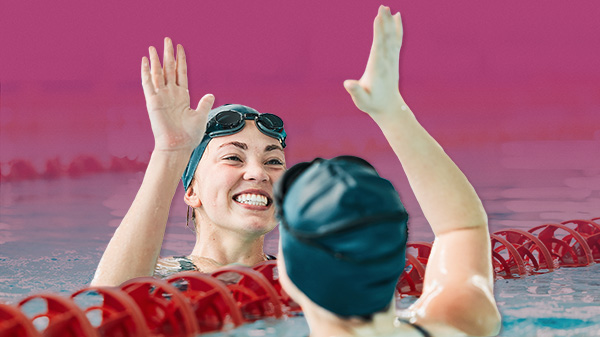 Two female swimmers in a pool high fiving.