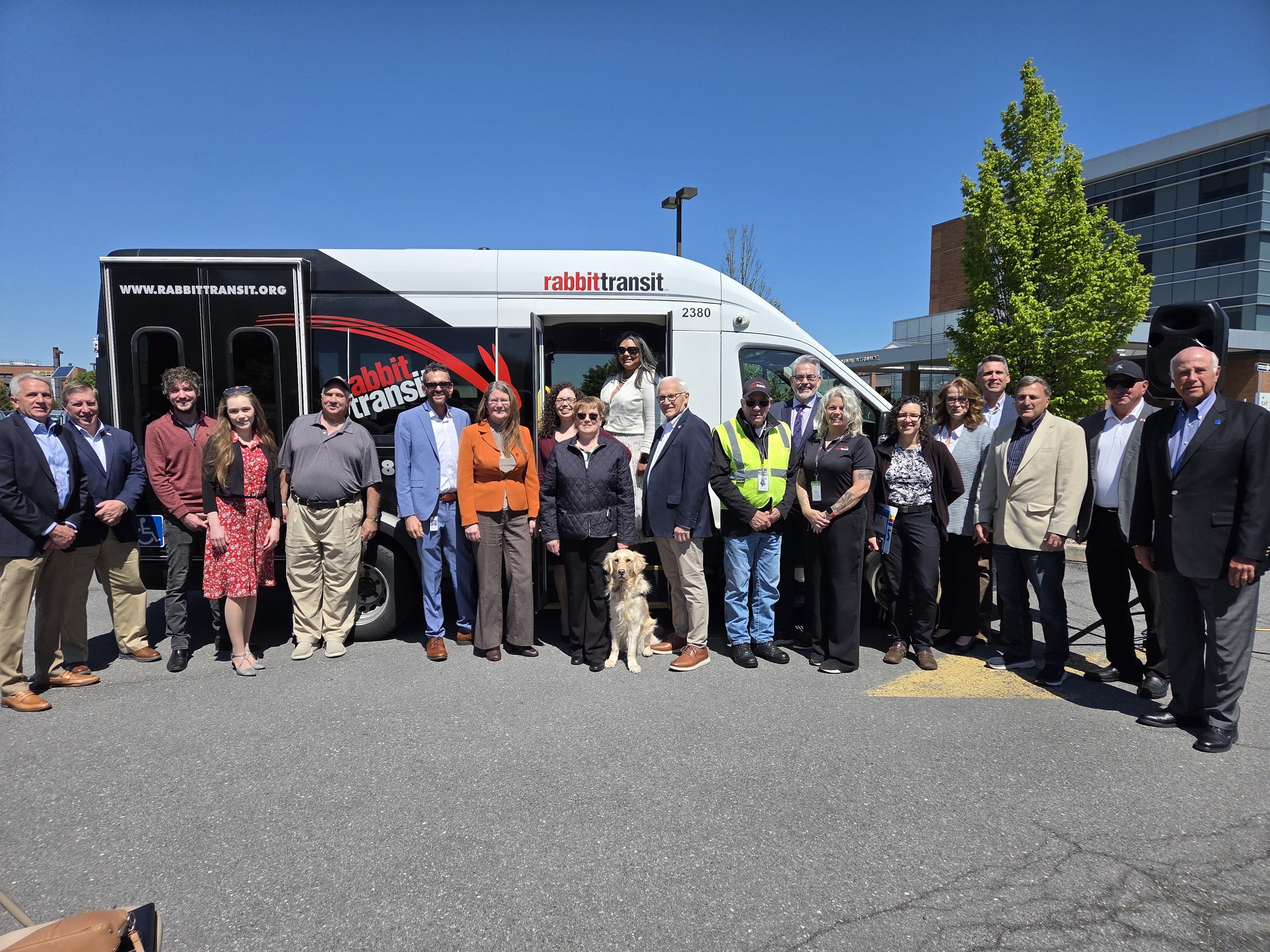 Sen. Yaw and a large group standing together outside in front of a RabbitTransit vehicle on a clear, sunny day, including a service dog positioned at the center.
