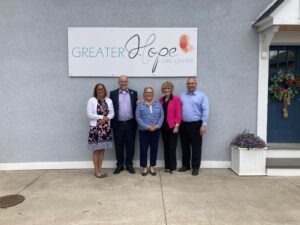 Five people standing in front of a building beneath a sign that reads “Greater Hope Care Center.” A flower planter sits to the right of the group.