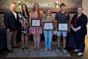 Seven people standing indoors at an event, with three young individuals holding framed award certificates. A sign reading “Bald Birds Brewing Co.” is displayed behind them.