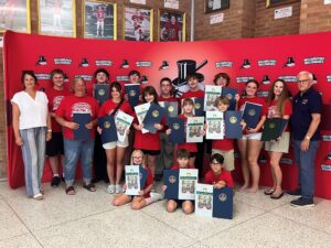 Sen. Gene Yaw and a group of students and adults pose together in front of a red Williamsport Millionaires backdrop, holding certificates and printed materials.