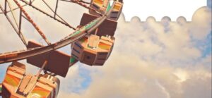A close-up view of a Ferris wheel shows several gondola cars against a cloudy sky.