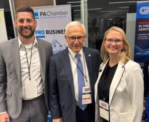 Sen. Gene Yaw and two people stand together smiling for a photo at a business event, with PA Chamber and aerospace innovation banners behind them.