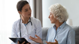 Senior woman takes a doctor at home telling about health complaints nurse writing personal information fill form attentively listens elderly patient. Healthcare, geriatric medicine, medical check-up
