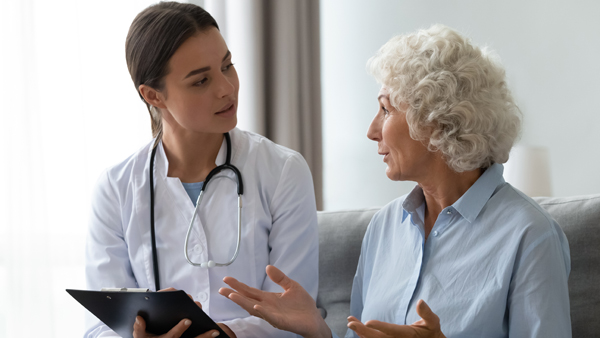 Senior woman takes a doctor at home telling about health complaints nurse writing personal information fill form  attentively listens elderly patient. Healthcare, geriatric medicine, medical check-up
