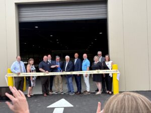 Sen. Yaw and A group of people stand in front of a large industrial building during a ribbon cutting ceremony, holding a long ribbon marked “Local Business. Local Success.”