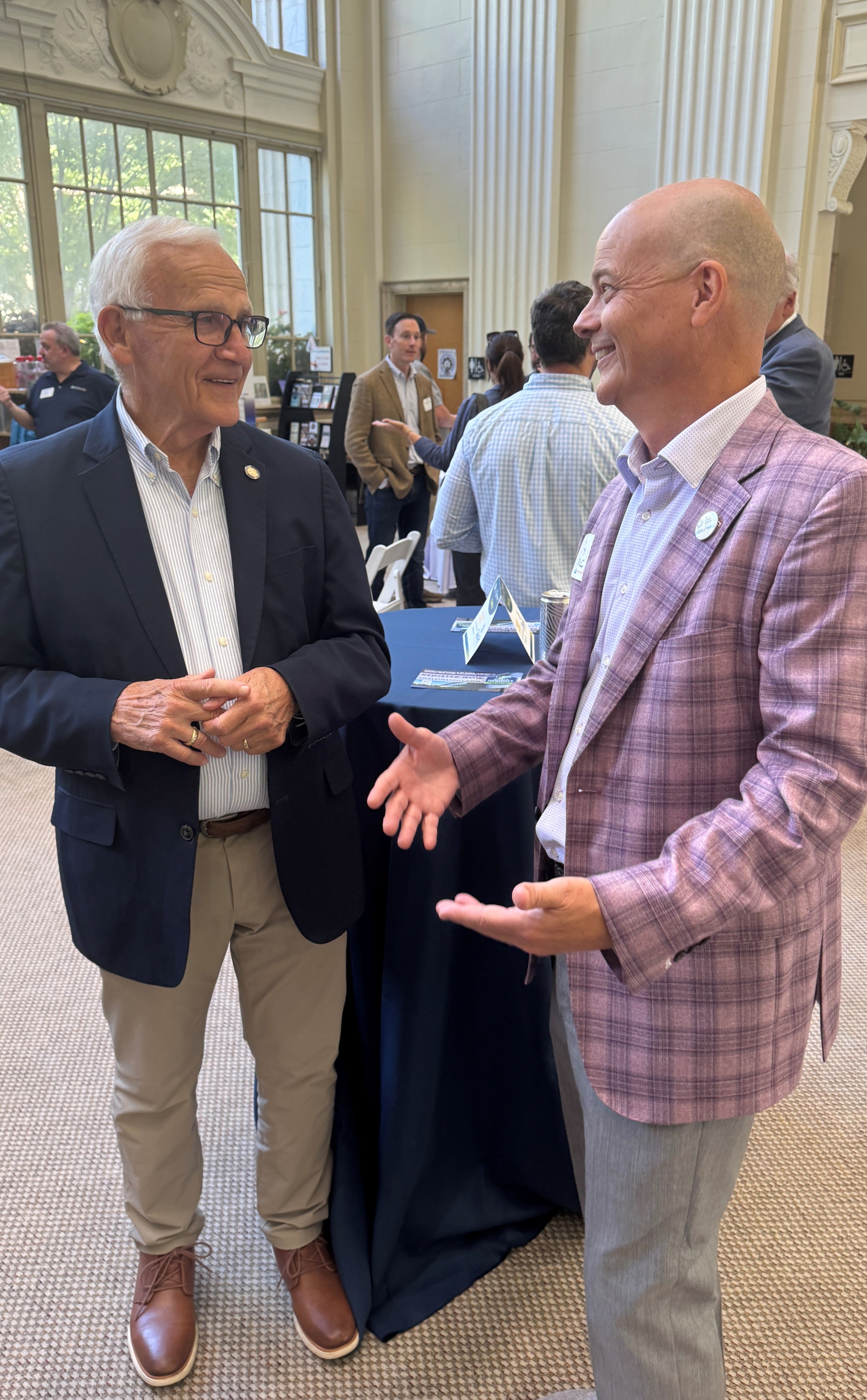 Sen. Yaw and another person standing indoors at a social or professional gathering, smiling and talking with each other. Several other attendees are visible in the background.