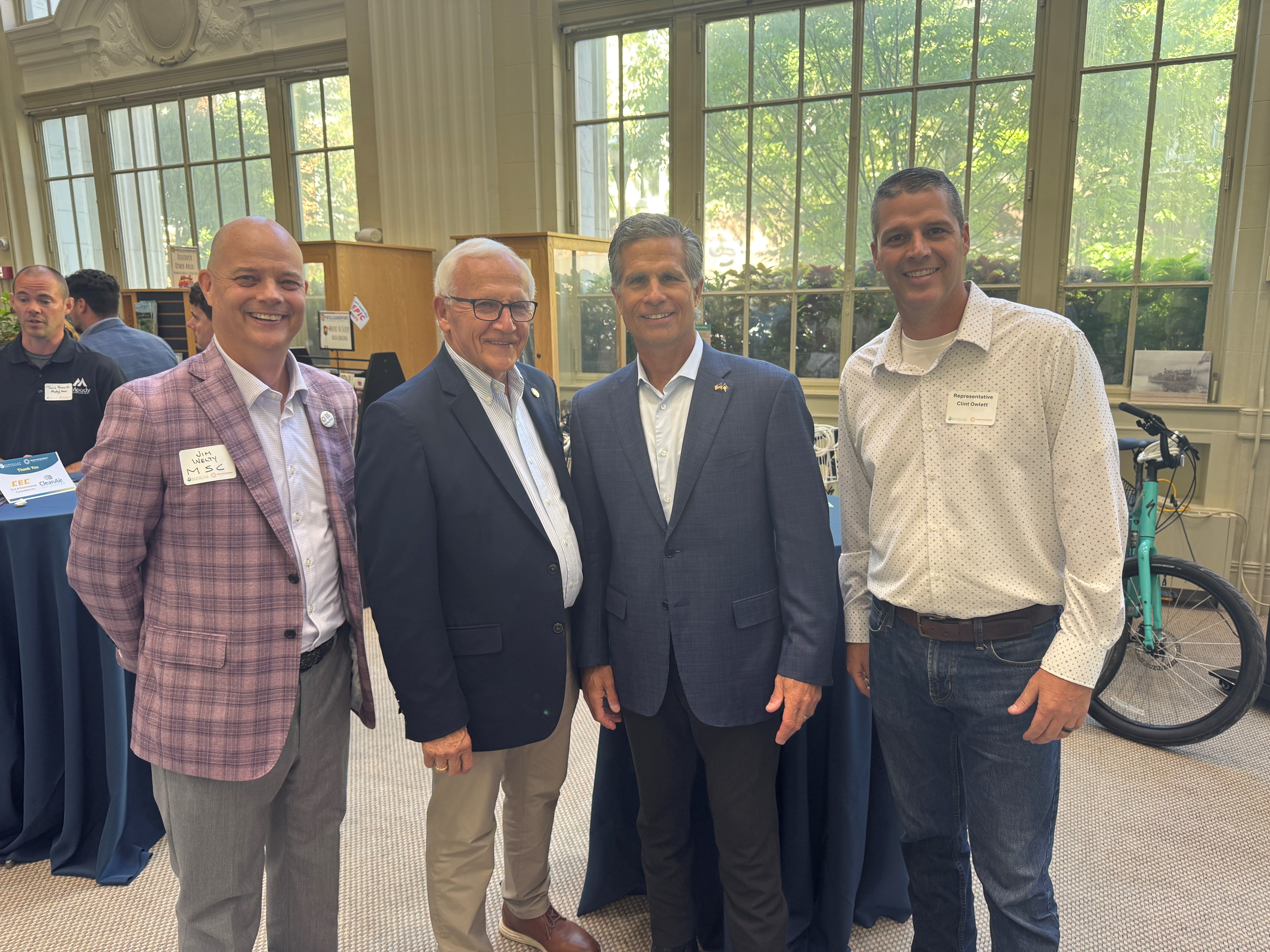 Sen. Yaw, Rep. Clint Owlett, Congressman Dan Meuser and another person standing side by side inside a large, bright room with tall windows, smiling at the camera. More attendees and tables are visible in the background.