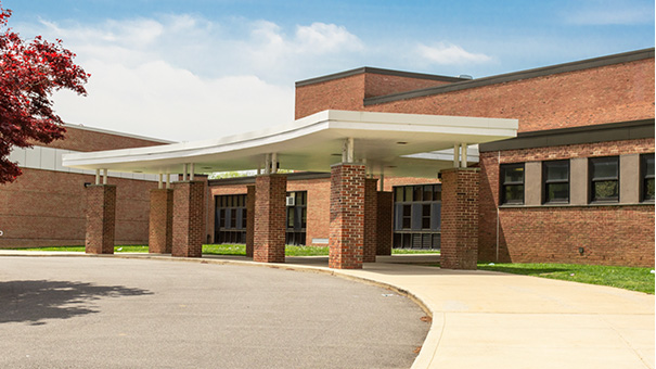 Sxterior of brick school building, front door entrance and part of paved parking lot